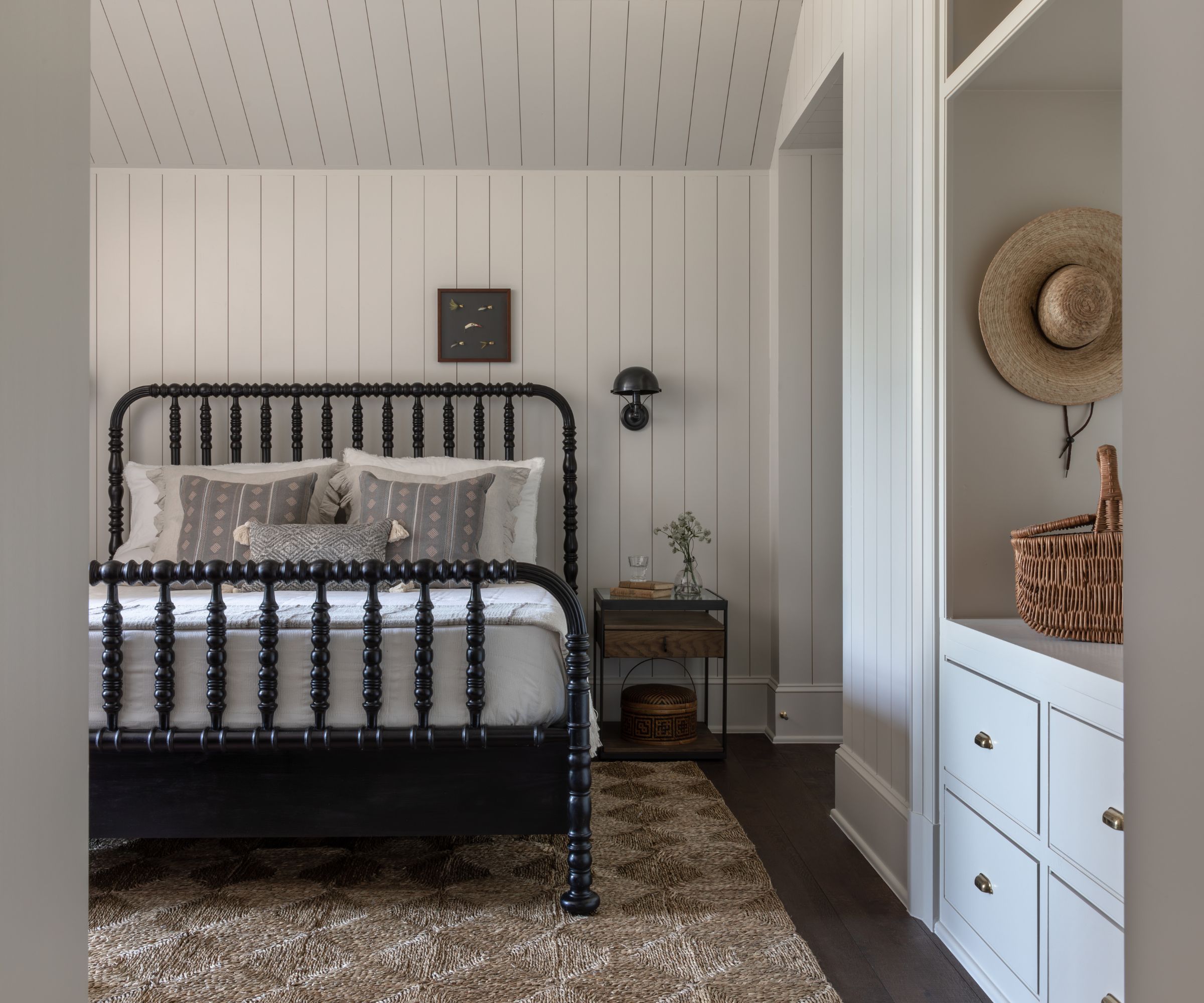 bedroom with white panelled walls and a sloped ceiling, a black double bed frame, and a textured beige rug