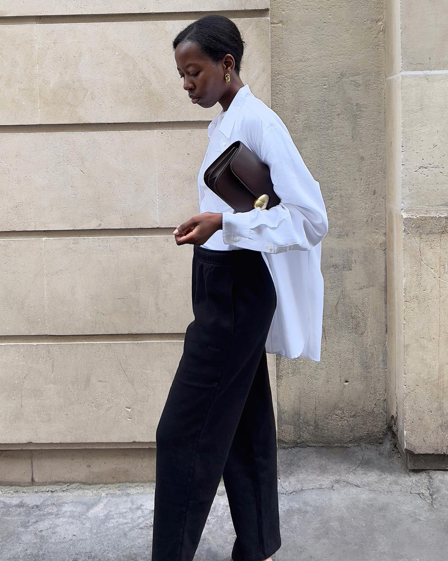 O influenciador de moda europeu Sylvie Mus usando uma camisa de botão branco polido, uma bolsa de embreagem marrom chique e calça preta.