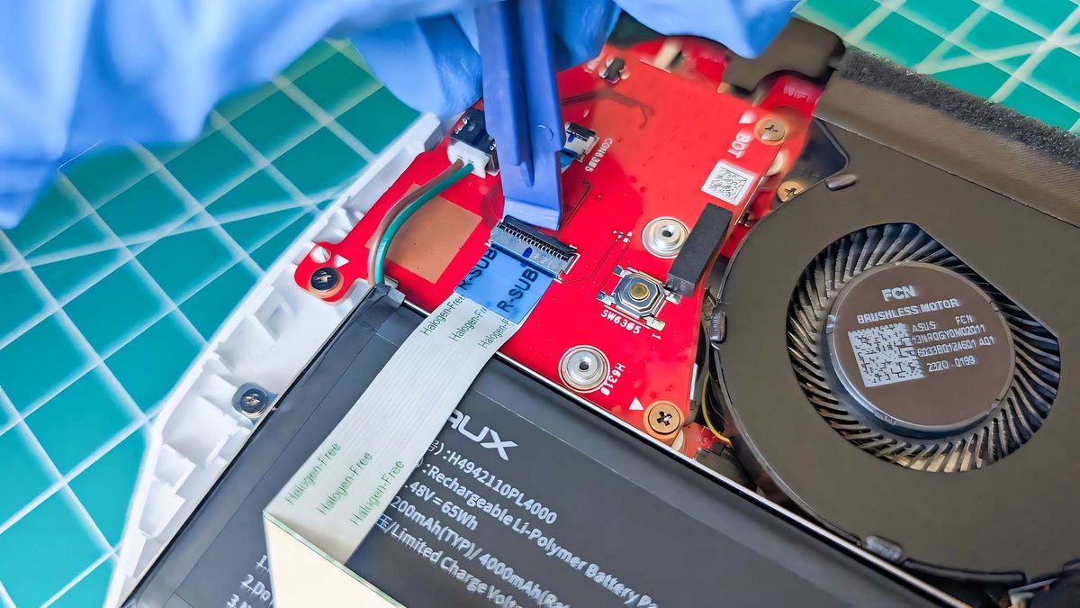 A gloved hand using the kit's included prying tool to unlatch a ribbon inside the ROG Ally.