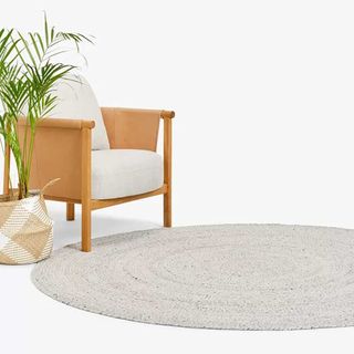 gray braided rug next to a plant and armchair to support the quiet luxury garden trend