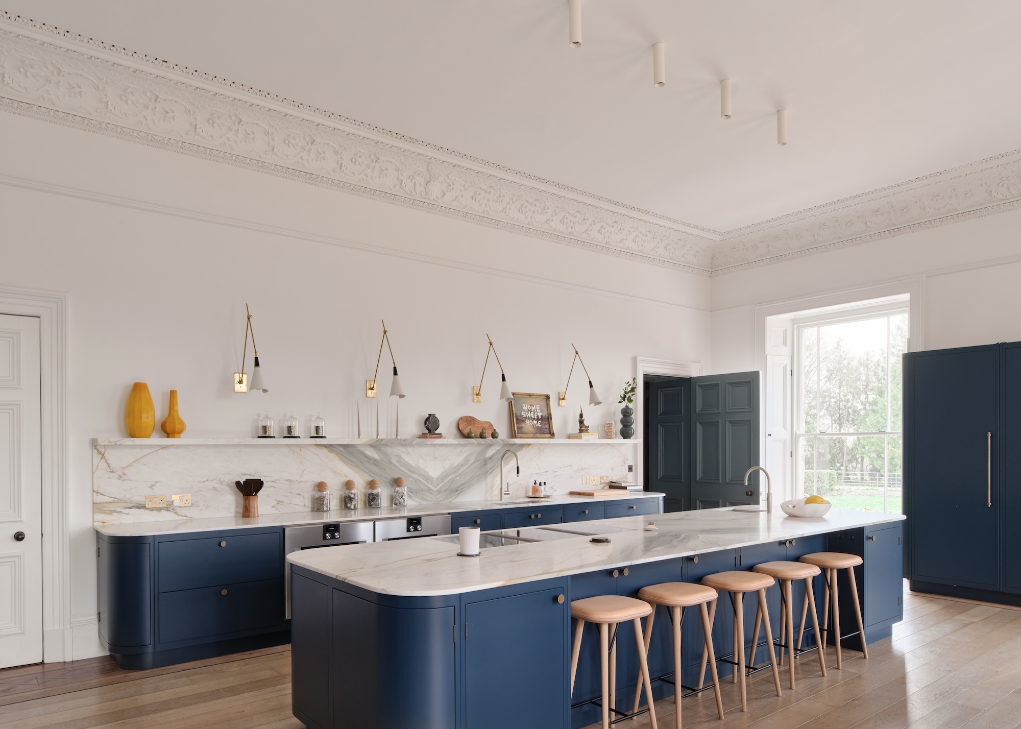 A navy blue kitchen island and lower cabinets with bar stools. The kitchen also has open shelves with lights above the shelves.