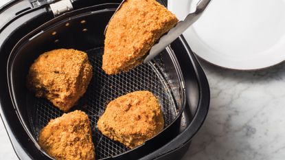 Air fried chicken in an air fryer picked up with tongs