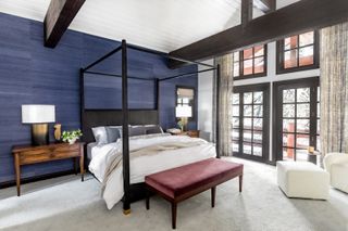 A modern bedroom with blue walls, a vaulted ceiling, and a four poster bedframe