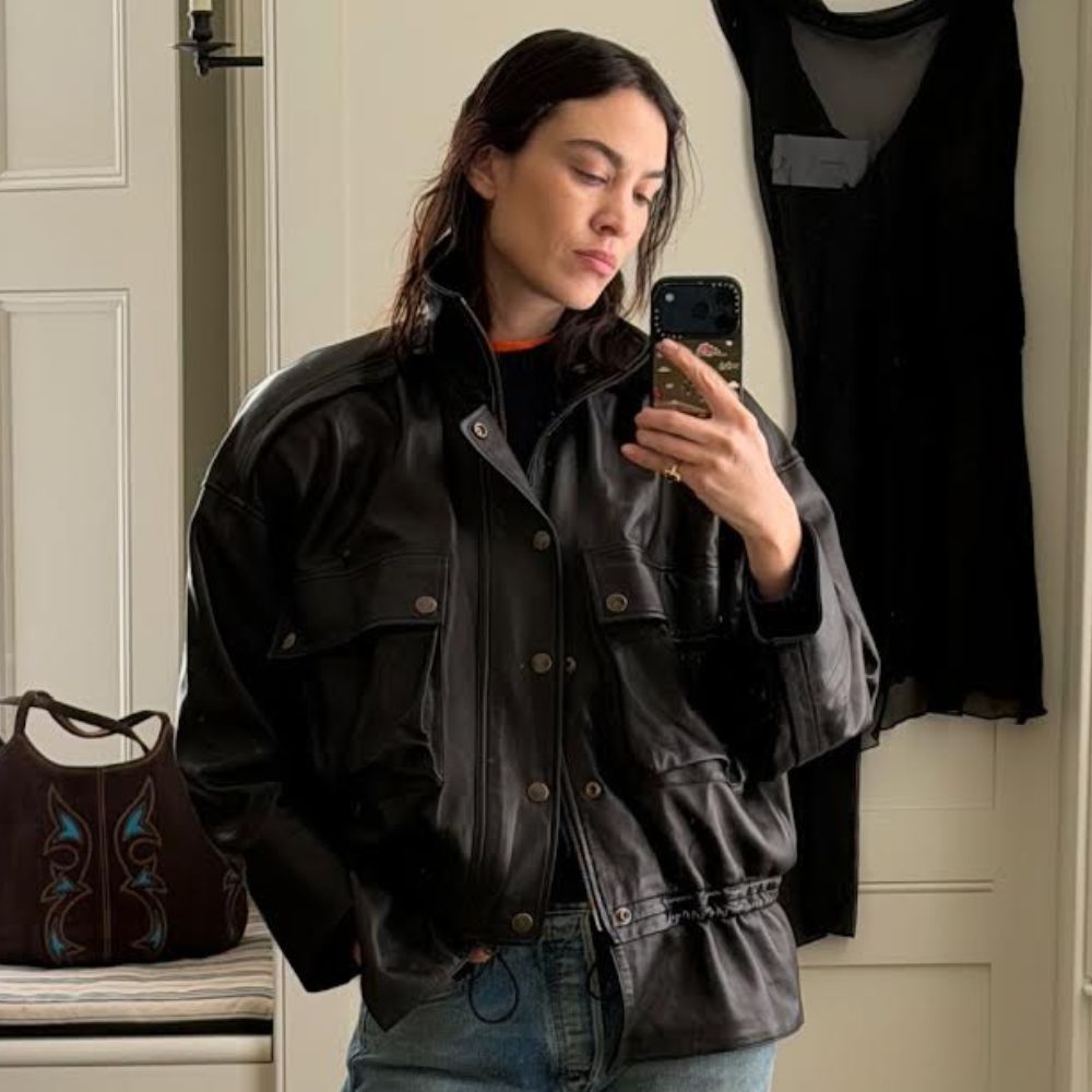 Alexa Chung takes a mirror selfie wearings straight-leg jeans with loafers and a cinch waist leather jacket.