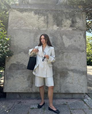 Woman wears linen blazer, linen shorts, sunglasses and handbag