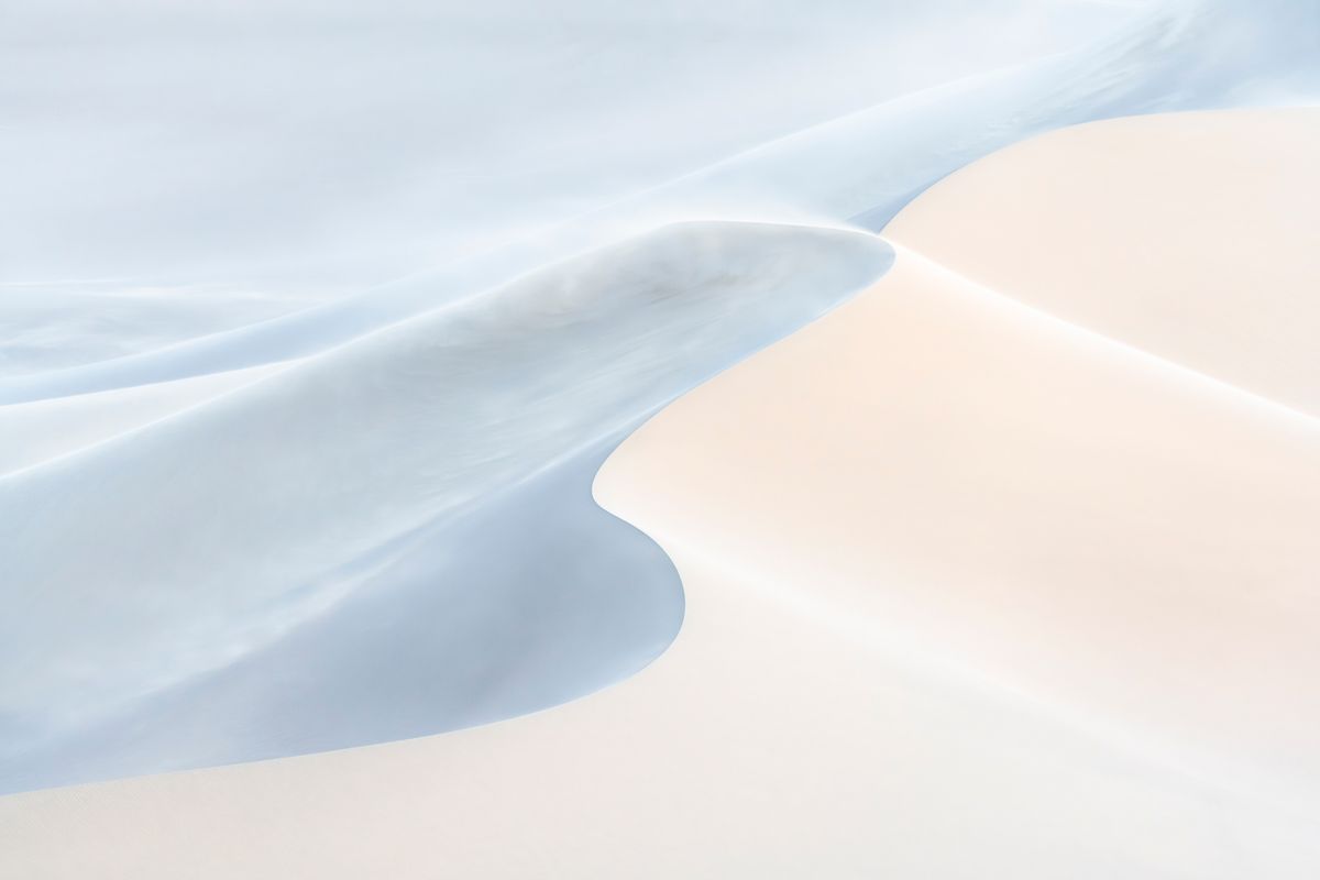 A serene abstract landscape featuring soft curves of light blue and pale sand, creating a tranquil and harmonious composition