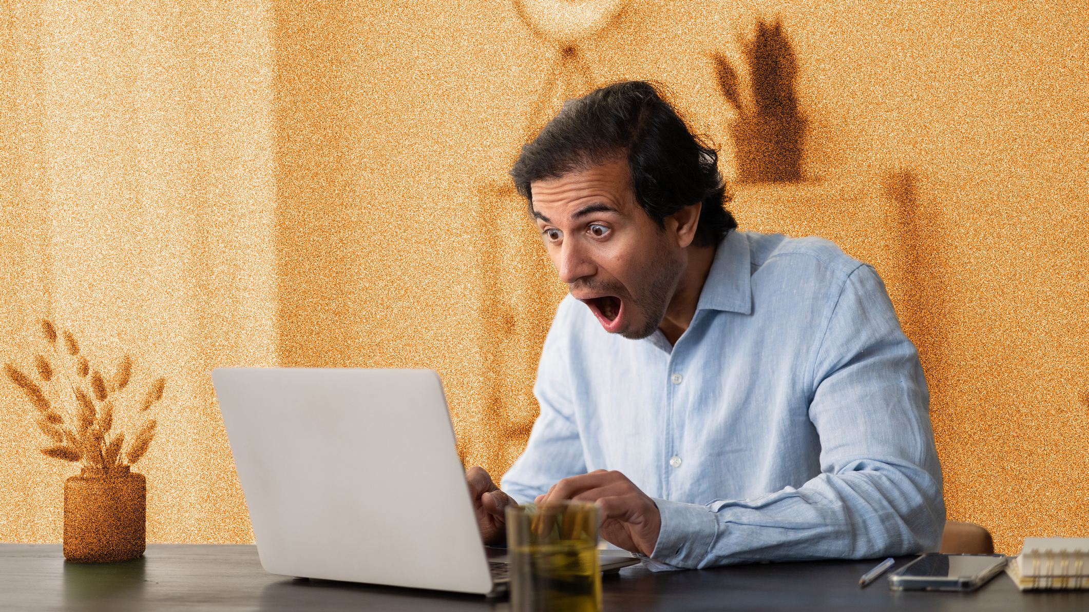Young man looking shocked, sitting at table looking at laptop. 