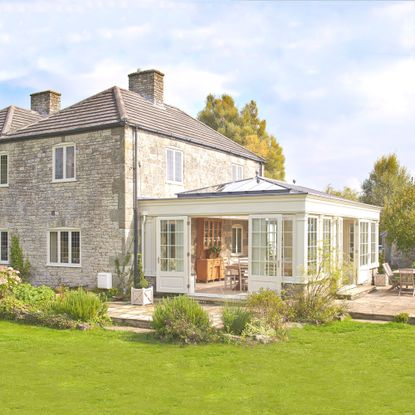 exterior image of stone house with cream oragnery with roof light leading onto a patio area and grass lawn