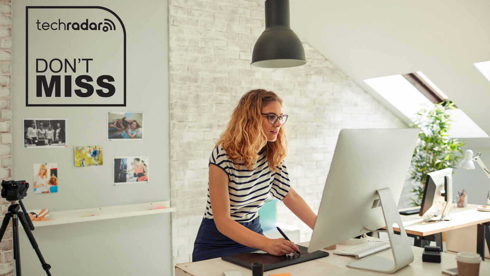 Woman standing at a desktop computer and drawing on a tablet in a loft-style space. The TechRadar logo and 