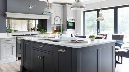 A modern kitchen with bifold doors, navy kitchen island and statement pendant light fixtures overhead