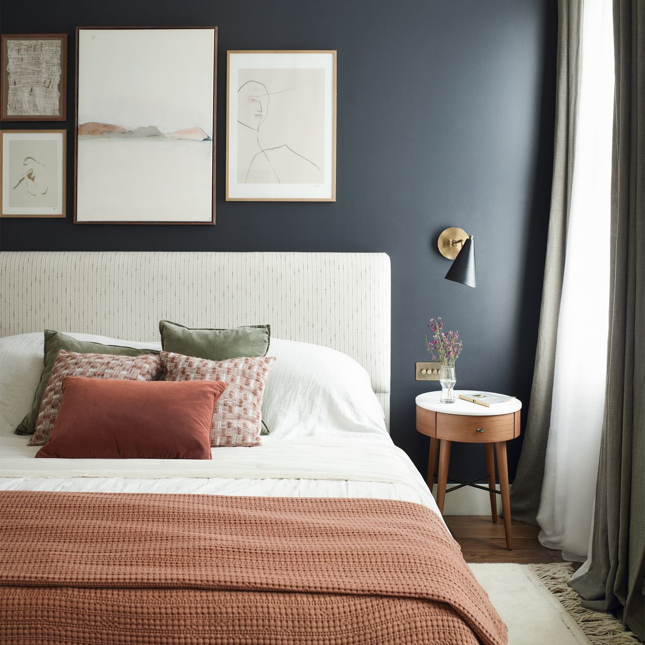 A navy bedroom with an upholstered bedframe and terracotta bedding