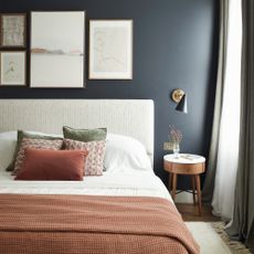 A navy bedroom with an upholstered bedframe and terracotta bedding