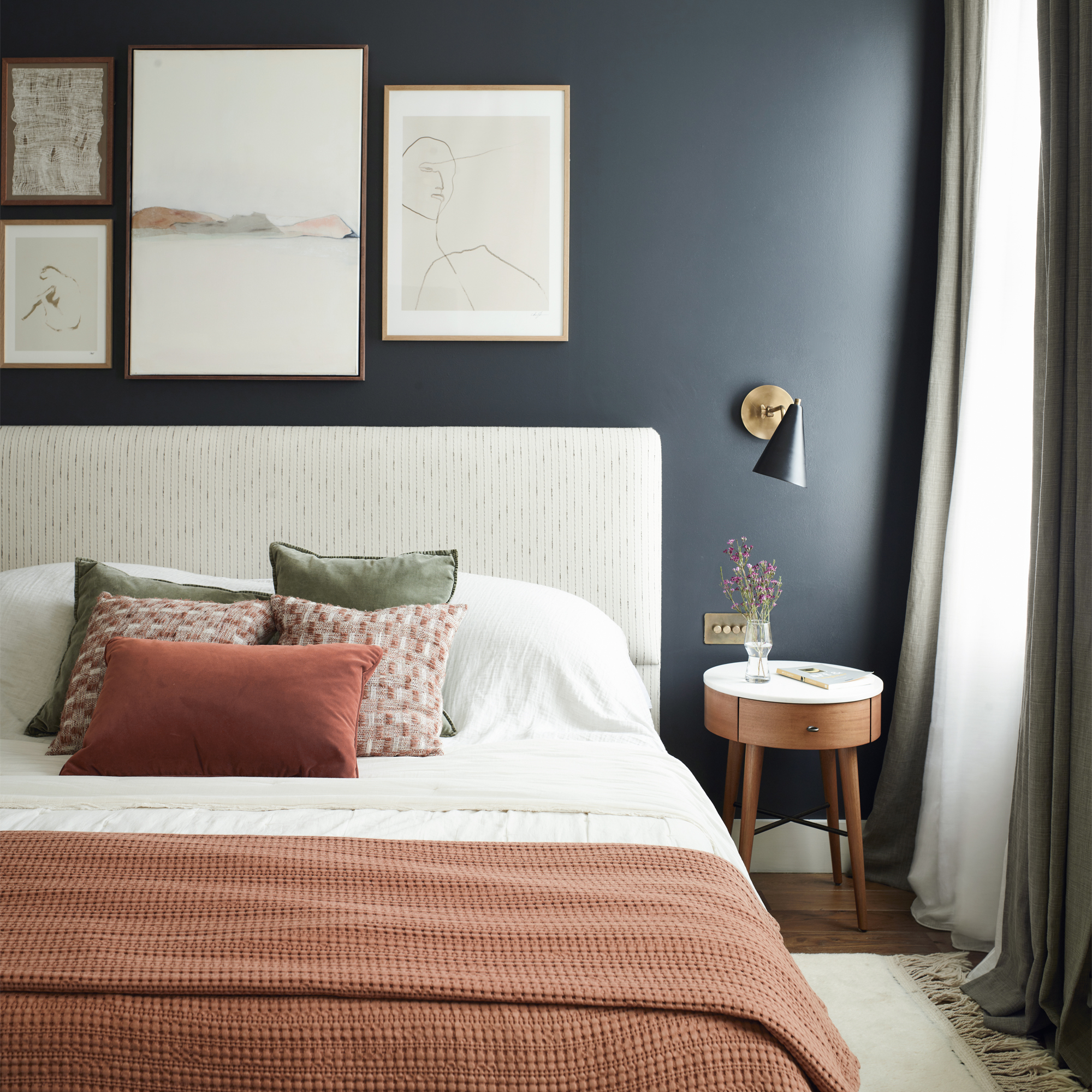 A navy bedroom with an upholstered bedframe and terracotta bedding
