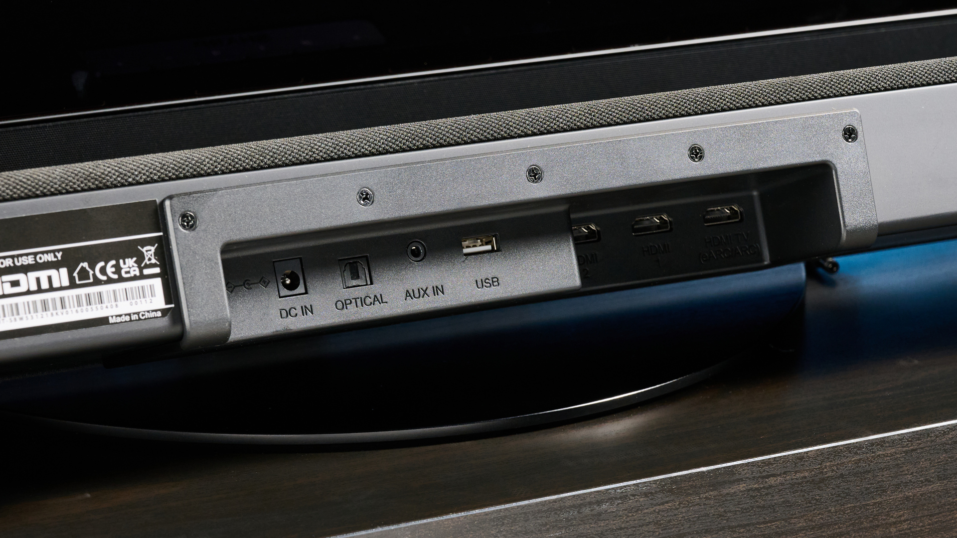 the Sharp 3.1.2 HT-SBW53121 Soundbar in black with a remote, subwoofer, against a blue background next to a panasonic TV