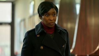 Cynthia Erivo stands in a lobby, wearing a long buttoned coat, in Luther: The Fallen Sun.
