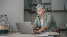 An older woman works on her laptop at her kitchen table.