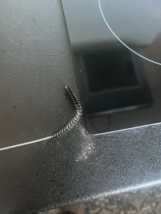 A black straw cleaning brush bent to fit under a stove top edge, cleaning out dust