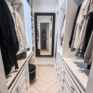 A white walk in dressing room with shelves on each side and a large mirror at the end