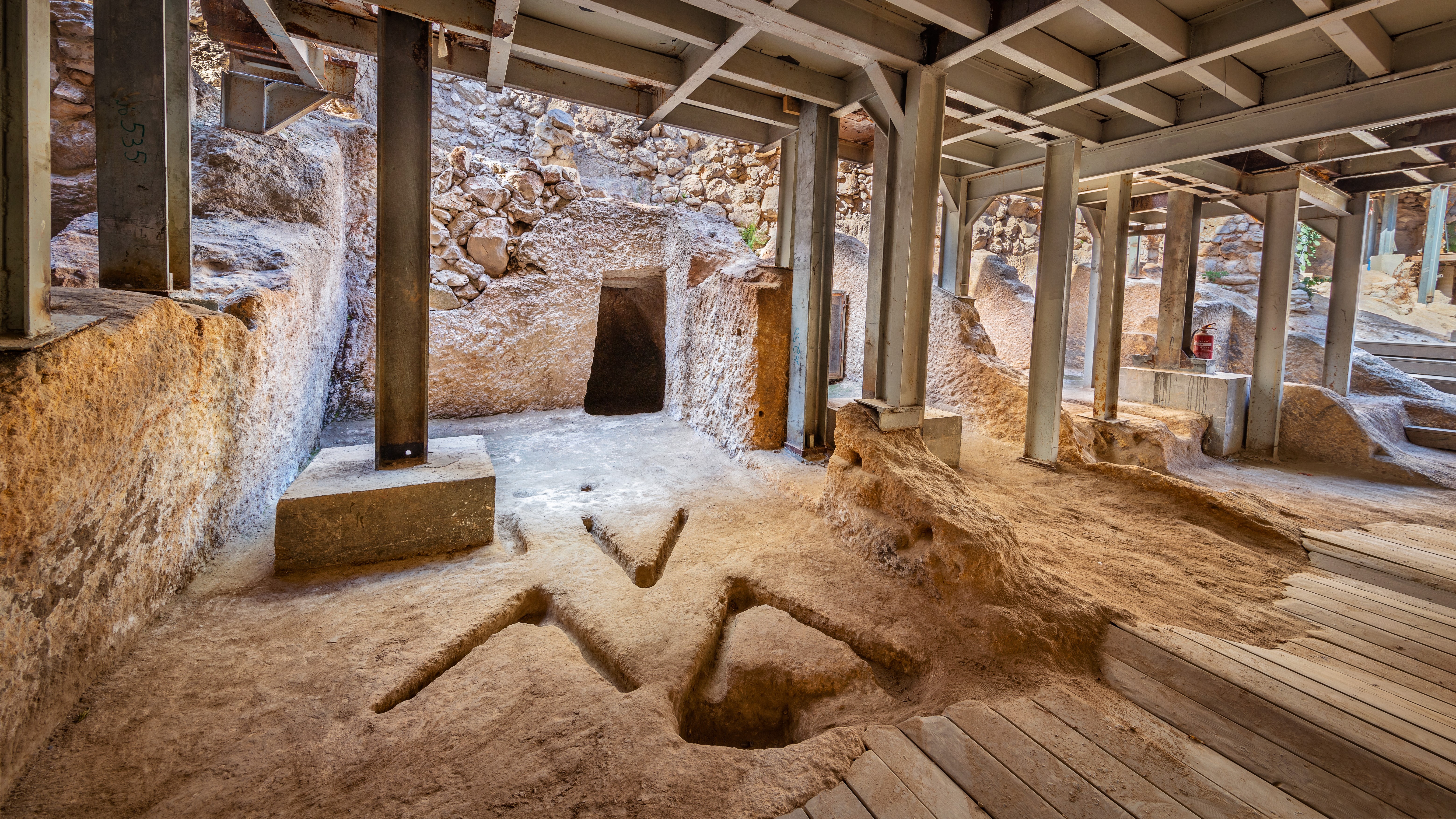 Excavation site of an ancient cultic complex in the City of David in Israel. The site is covered with a temporary roof. We see three V-shaped grooves in the ground.