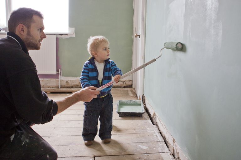 toddler son helps dad roll paint onto a wall