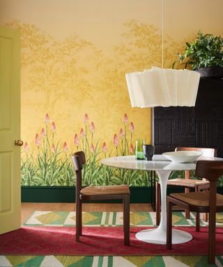 Bright dining room with wall mural on one side, yellow design with flowers growing up from the ground, dining table, chairs, pendant light, patterned rugs
