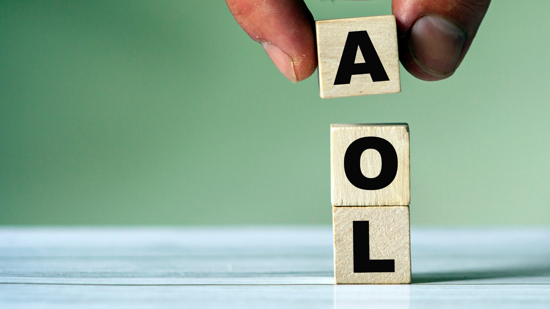 A stock photo of a hand placing a wooden block to spell out the initialism &#039;AOL&#039;