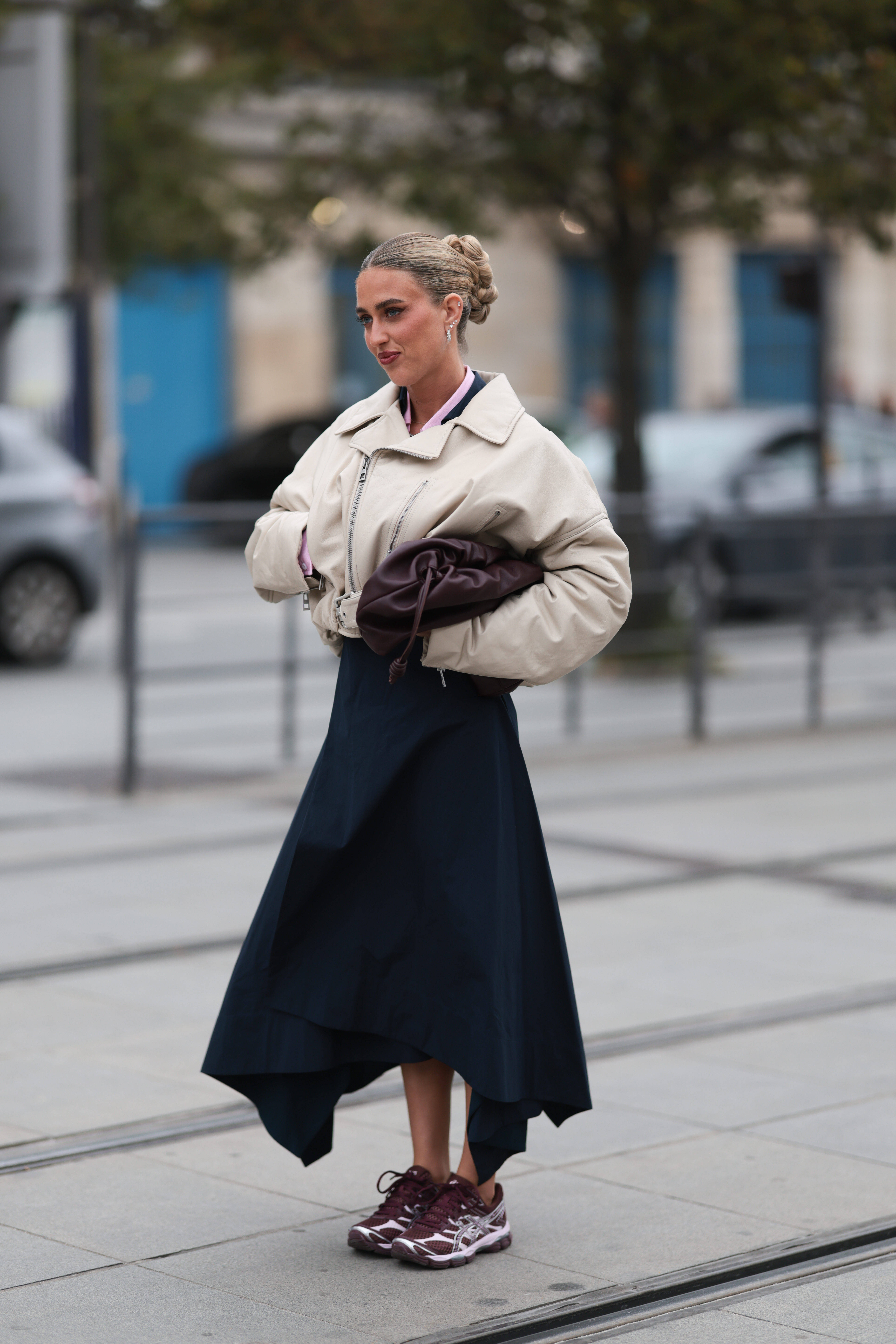 A woman wears a skirt, burgundy sneakers (one of the biggest sneaker color trends of 2026), and a beige bomber jacket.