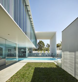 Side-view of the exterior of a residential home showing the green lawn, swimming pool and a seating area