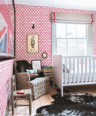 A baby girl nursery idea with white and red wallpaper, white crib, taupe patterned armchair and animal skin rug.