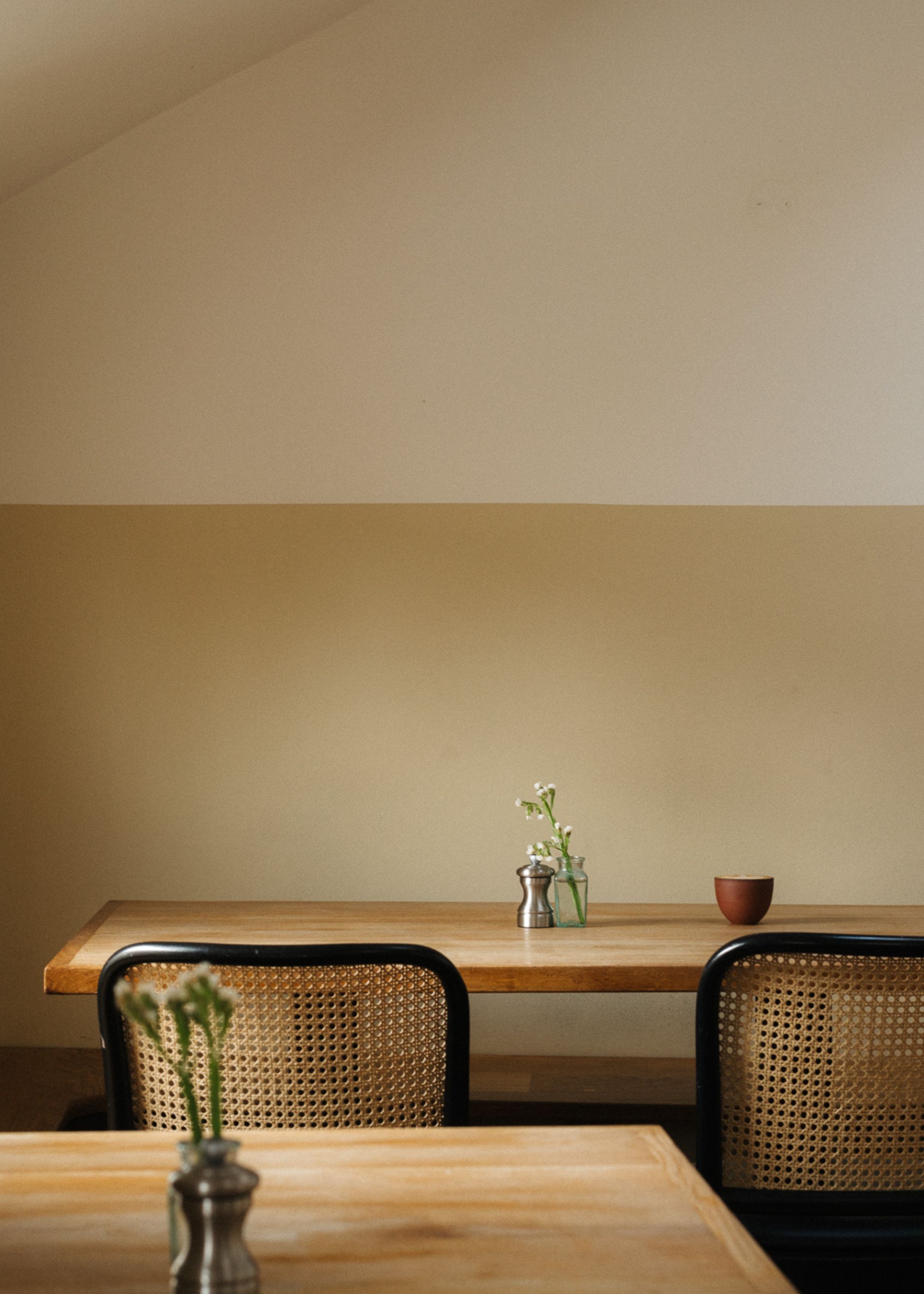 A dining room with dark sand paint on the lower wall, and a soft white on the upper half. Two wooden tables with rattan chairs.