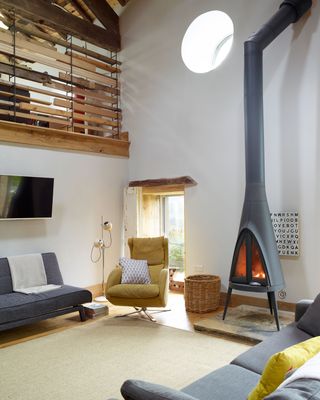 A barn living room owned by Sophie and Bob Waiting with vintage finds and salvaged treasures including yellow accent chair, modern stove fireplace and grey sofa