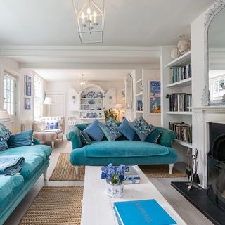 Two blue couches next to coffee table with a white pot and blue flowers next to fire place