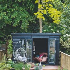A black garden outbuilding with a tree behind it