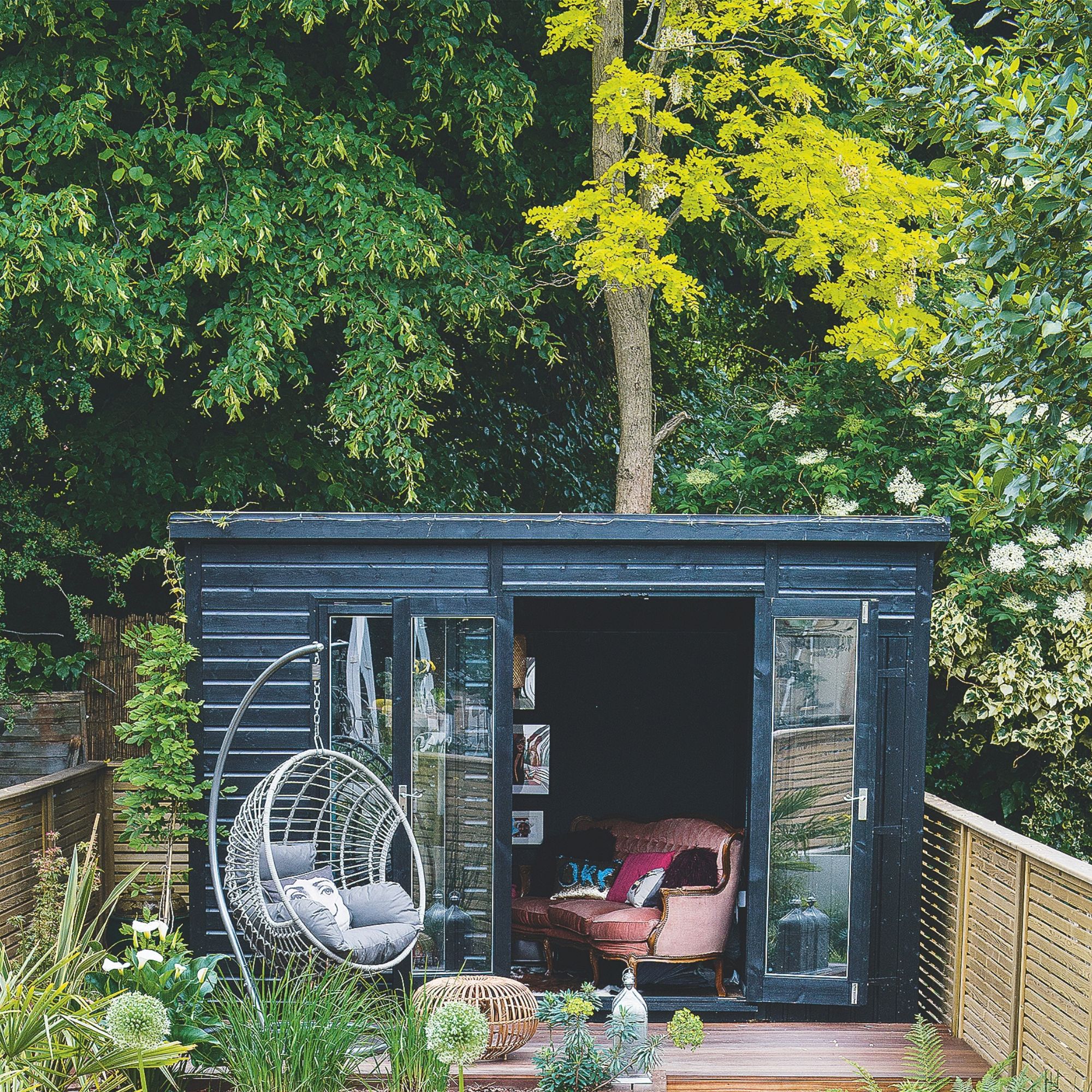 A black garden outbuilding with a tree behind it