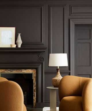 A black color drenched living room with bold orange/light brown arm chairs. a fireplace mantle with frames on top