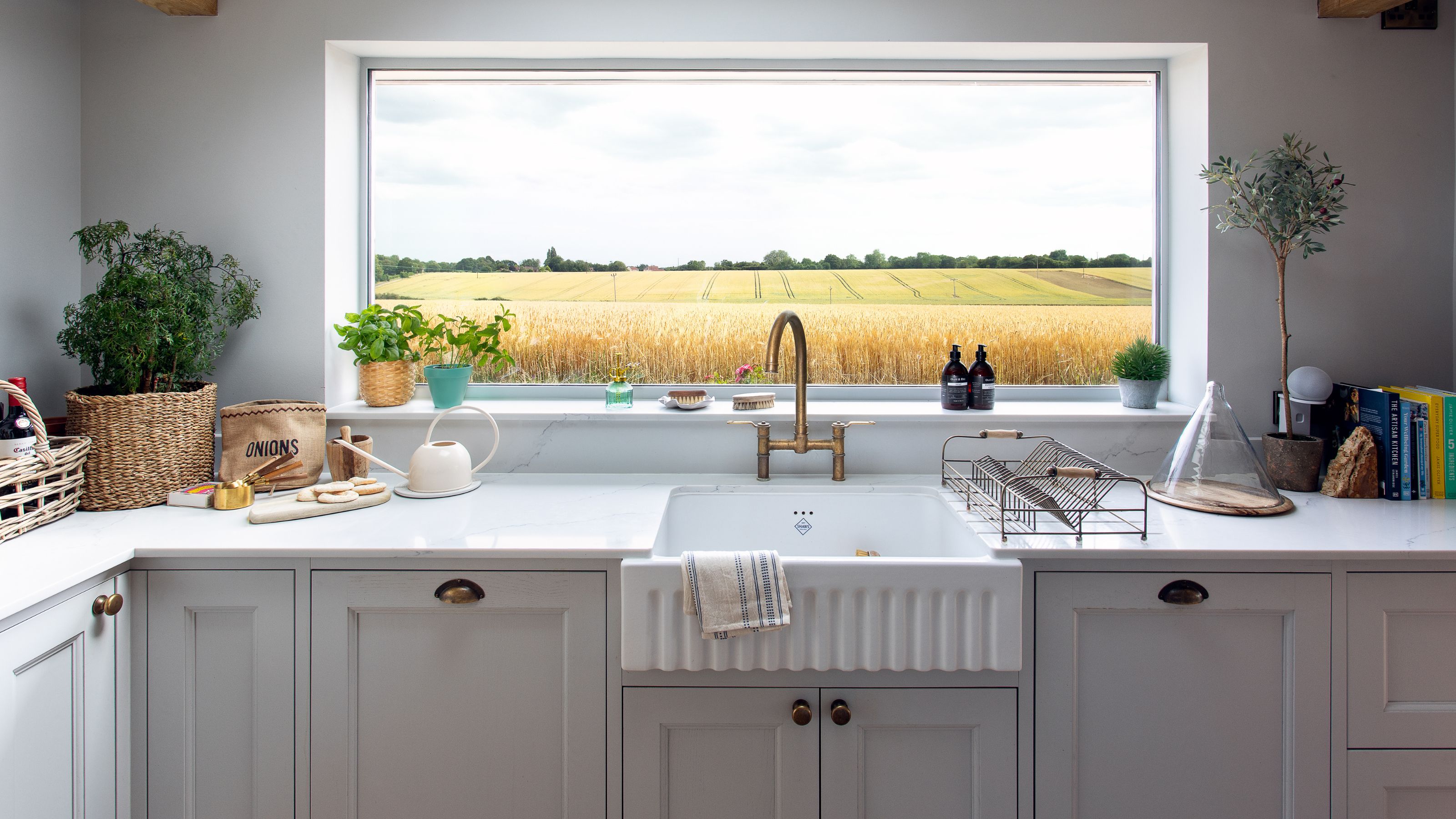 Kitchen with white cabinets and a ceramic sink, with a large picture window in front looking over yellow fields