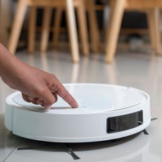 white robot vacuum on a glossy grey tiled floor with hand reaching in to press button