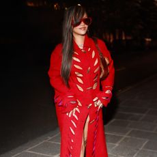 Rihanna wearing a red cutout coat from Dior, white Loewe heels, and red sunglasses.