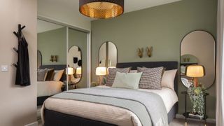 A showroom bedroom with green walls and and symetrical mirrors and lighting either side of the bed