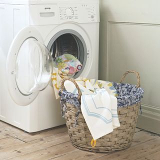 White washing machine in a white room, with clothes falling out of it and into a laundry basket