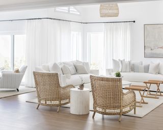 Living room with wood floor, rattan armchairs and white couches, neutral rug and white walls