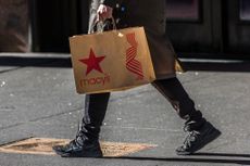 Person walking on sidewalk holding a Macy's shopping bag. 