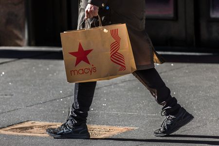 Person walking on sidewalk holding a Macy's shopping bag. 