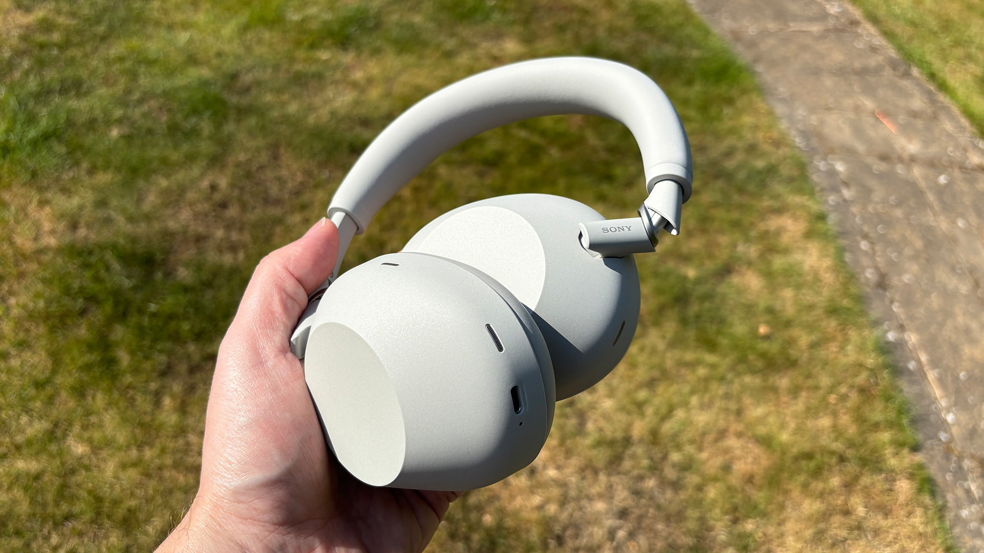 Sony WH-1000XM6 over-ear headphones held in hand above lawn