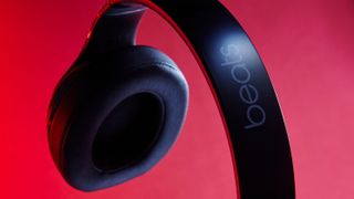 En närbild på ett par svarta Beats-hörlurar visas upp mot en röd bakgrund.
