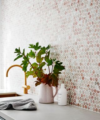 A laundry room with hexagonal tile feature wall decor, brass-colored faucet, potted plant in white vase and grey kitchen teatowel
