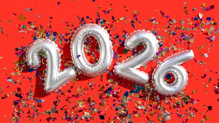 Silver balloons spell out 2026 against a red background and confetti.