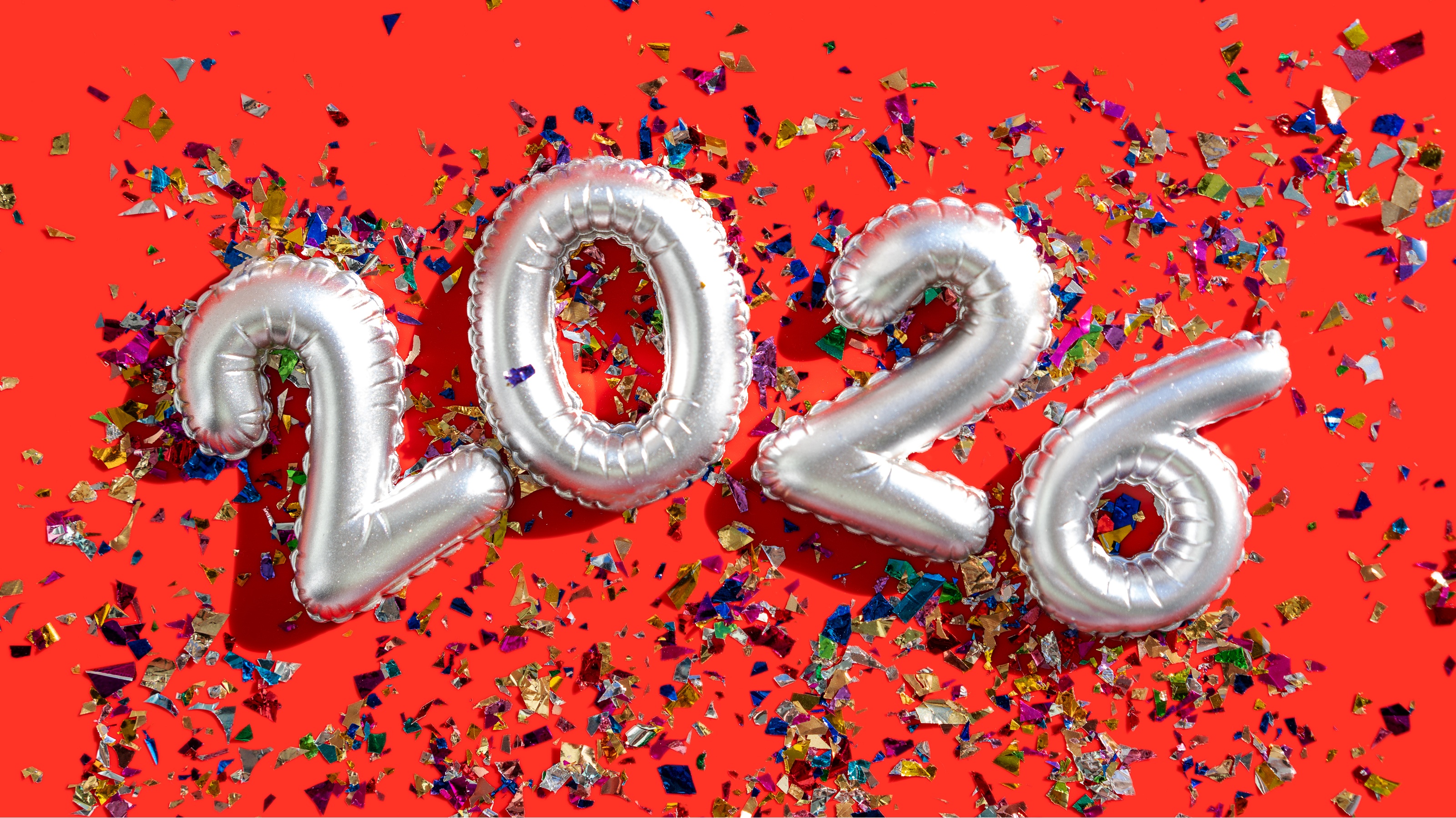 Silver balloons spell out 2026 against a red background and confetti.