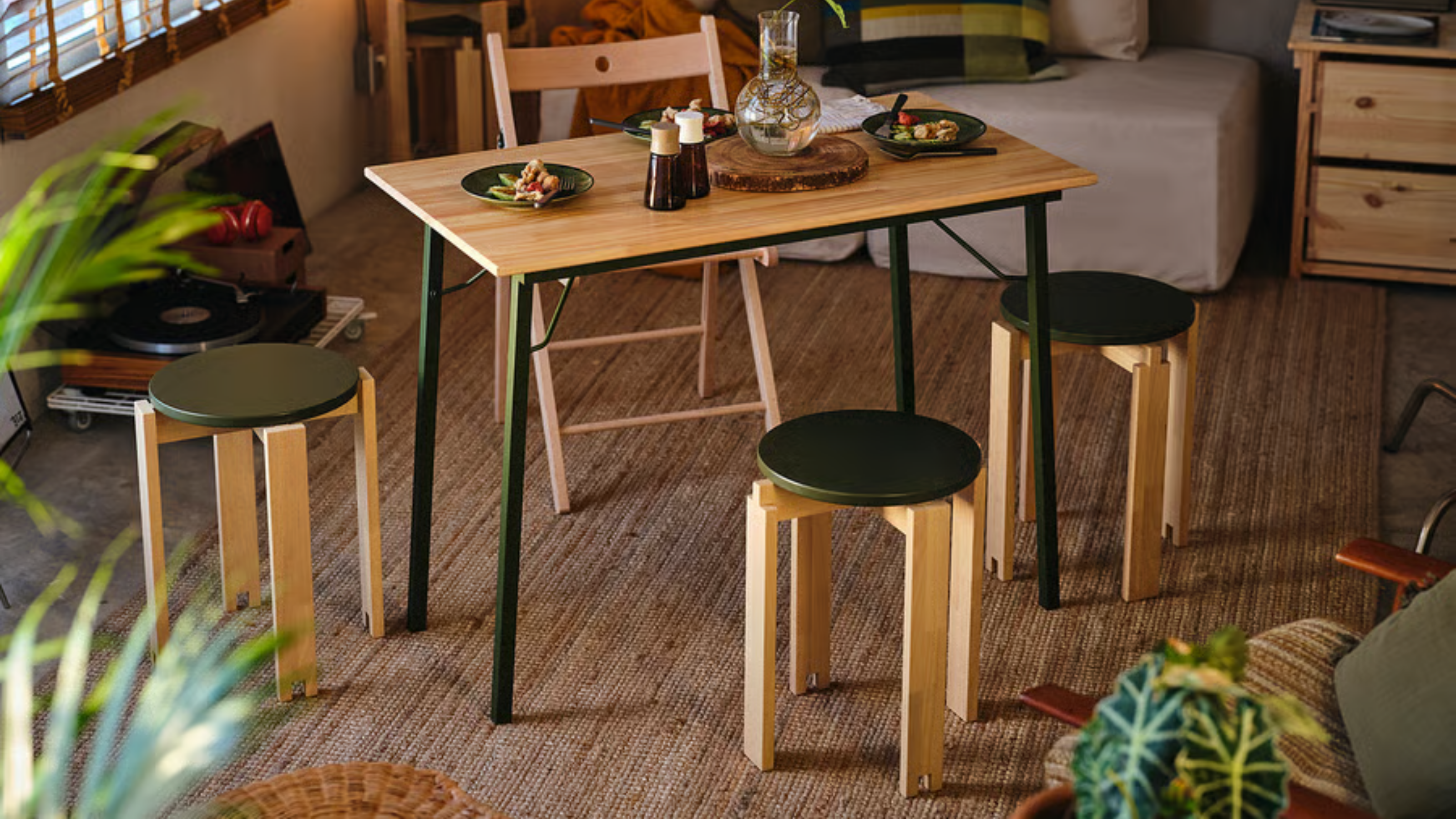 a living room with a small table, three stools, a folding chair, and a jute rug