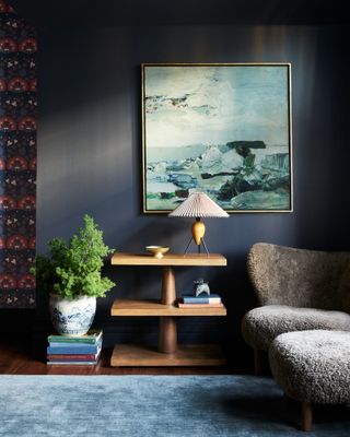 Living room with dark wood flooring, dark blue walls, lighter blue rug and mid-tone wood side table